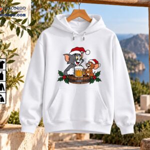 Christmas cartoon artwork featuring a gray cat and brown mouse in Santa hats sharing golden beer mugs on a holly-decorated wooden barrel